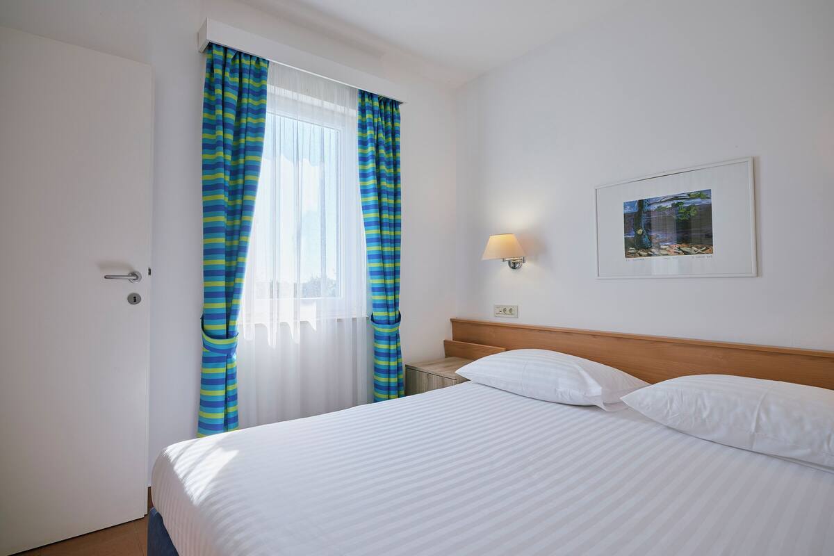 Ein Hotelzimmer mit einem Bett, einem Nachttisch, einer Lampe und einem gerahmten Bild an der Wand.