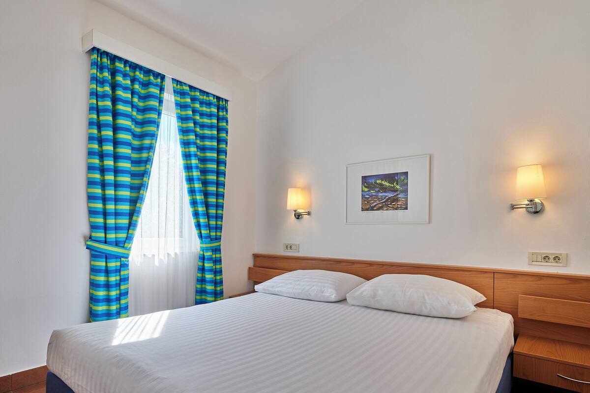 Ein Hotelzimmer mit Bett, Vorhängen, Wandleuchten und einem gerahmten Bild.