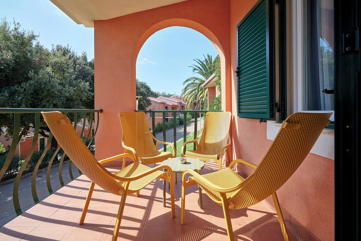 Ein Balkon mit gelben Korbstühlen und einem Tisch, der auf eine Straße mit Palmen und Gebäuden blickt.