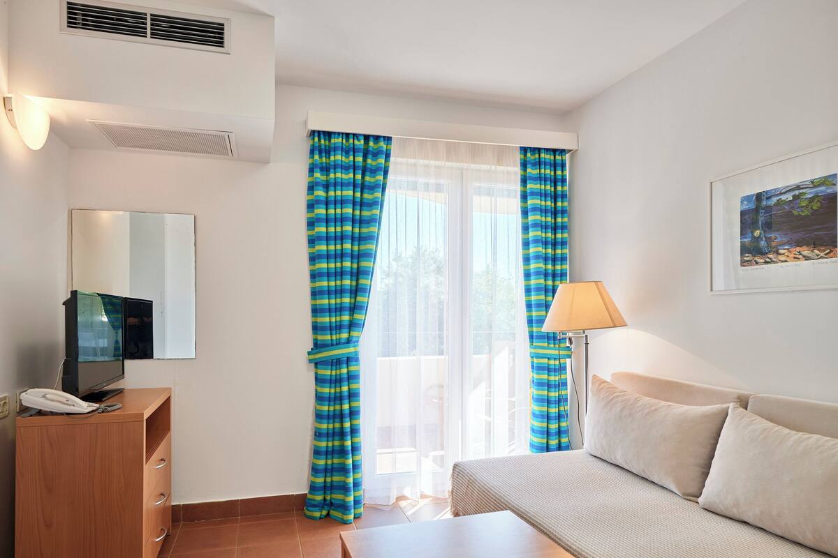 Ein Hotelzimmer mit Bett, Schreibtisch, Lampe, Telefon und Vorhängen.