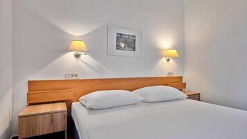 A neatly made bed with white linens and two pillows, flanked by wooden nightstands with lamps.