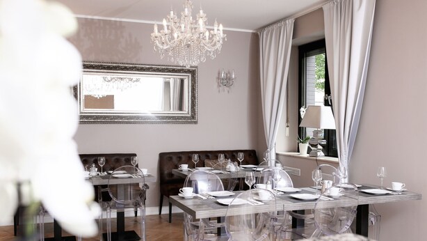 A dining area with a chandelier, a large mirror, and a window with curtains. - Hotel Lux (Düsseldorf)