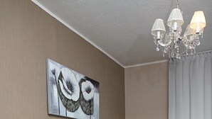 A neatly made bed with a grey headboard, a bedside table with a lamp, and a chandelier above. - Hotel Lux (Düsseldorf)