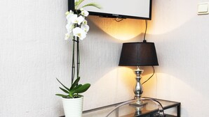 A hotel desk with a framed sign, a lamp, a potted plant, and a clear chair. - Hotel Lux (Düsseldorf)
