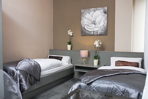 Habitación de hotel con dos camas, una mesita de noche con lámpara, una obra de arte en la pared y dos plantas en macetas.