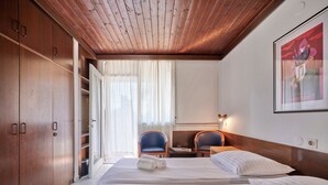 Habitación de hotel con dos camas, armario de madera, escritorio, sillas y un cuadro en la pared.