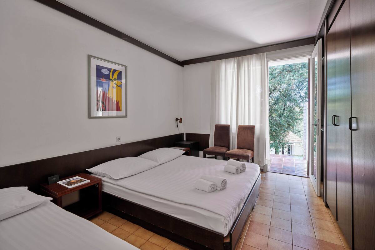 Une chambre d’hôtel avec un grand lit, un lit plus petit, un bureau, une chaise et une armoire.