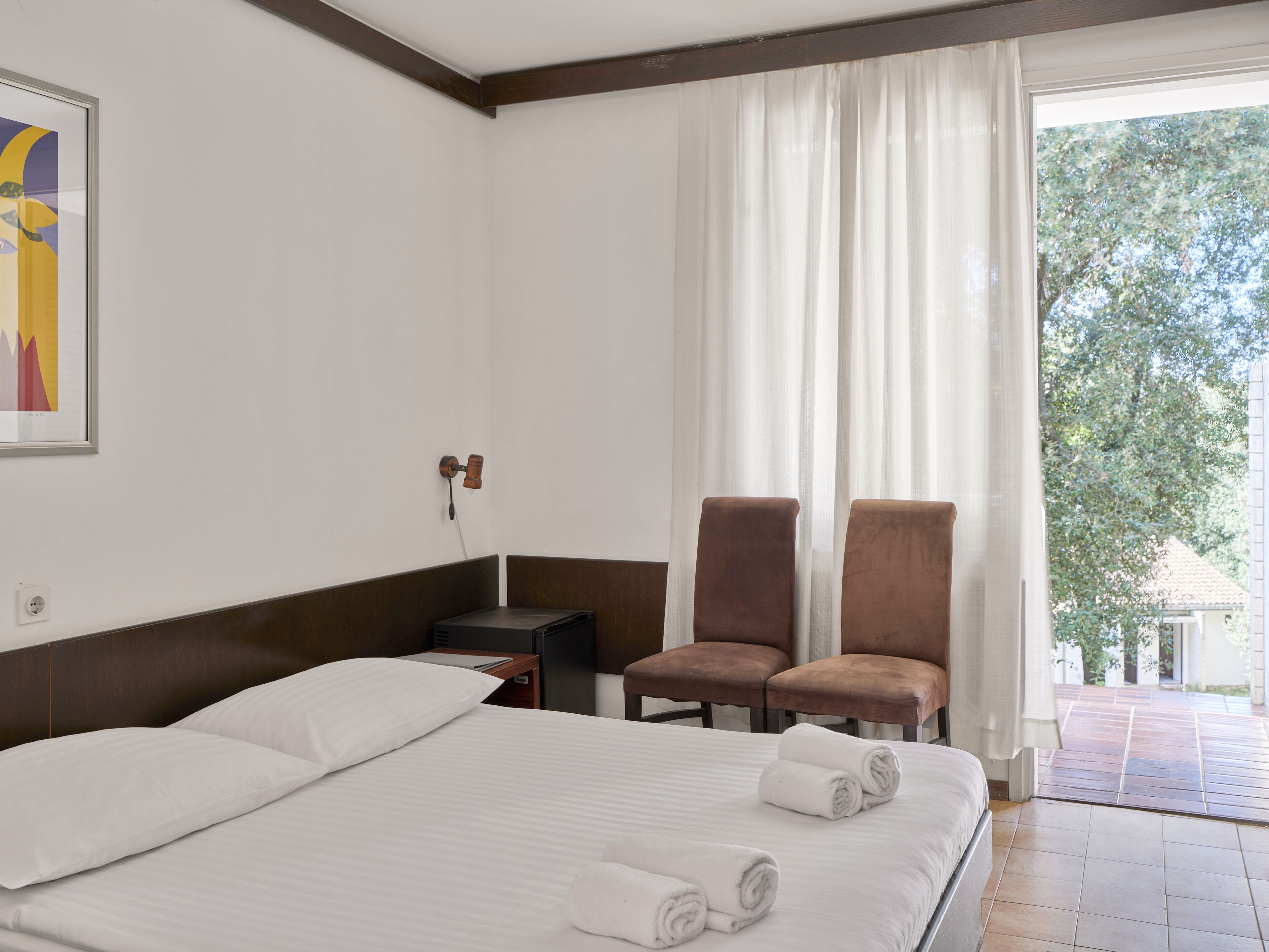 A hotel room with a bed, two chairs, a nightstand, and a window with curtains.