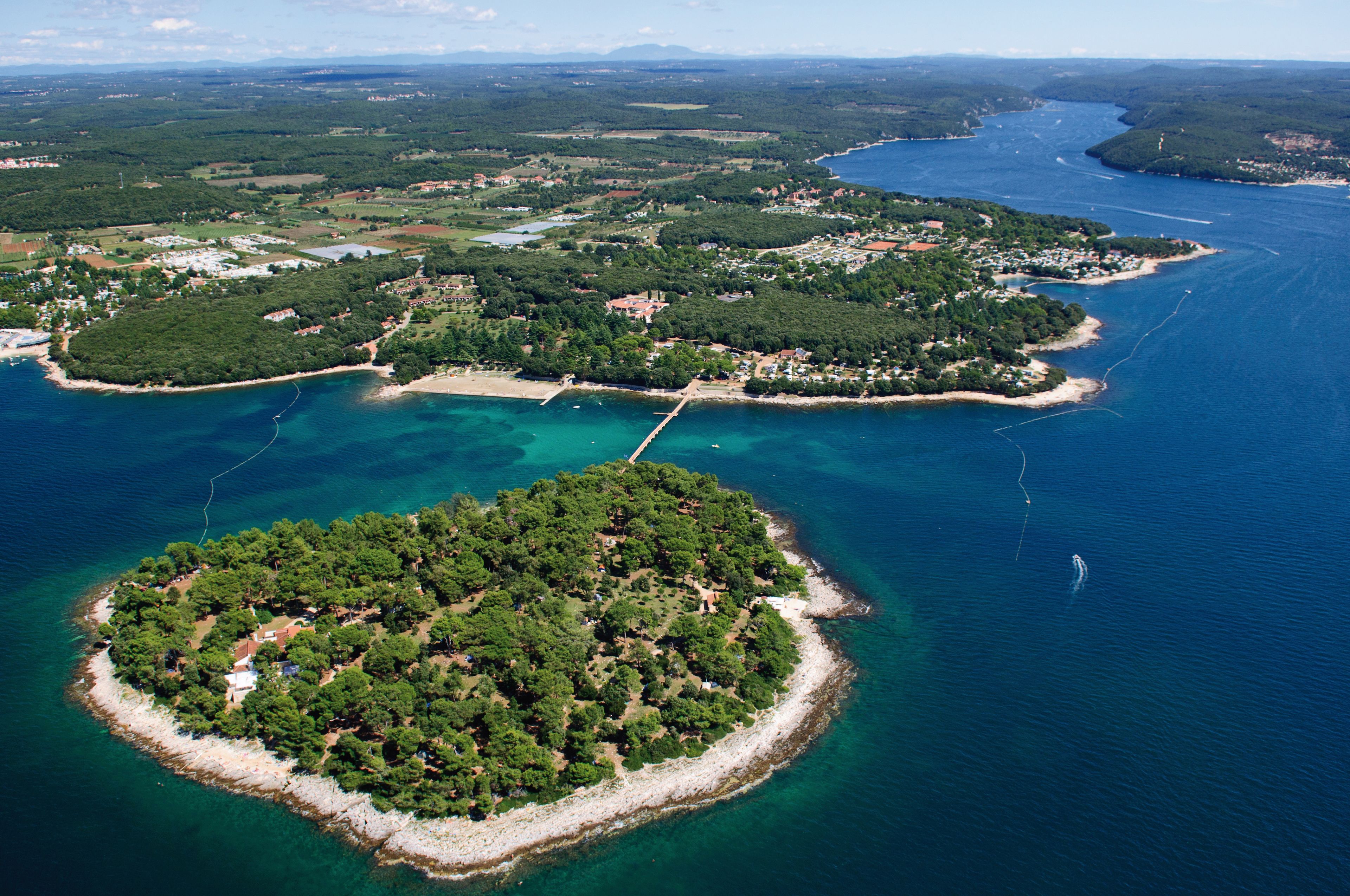 Une vue aérienne d’une zone côtière comprenant de nombreuses îles, des eaux d’un bleu limpide et un paysage mêlant zones boisées et zones aménagées.