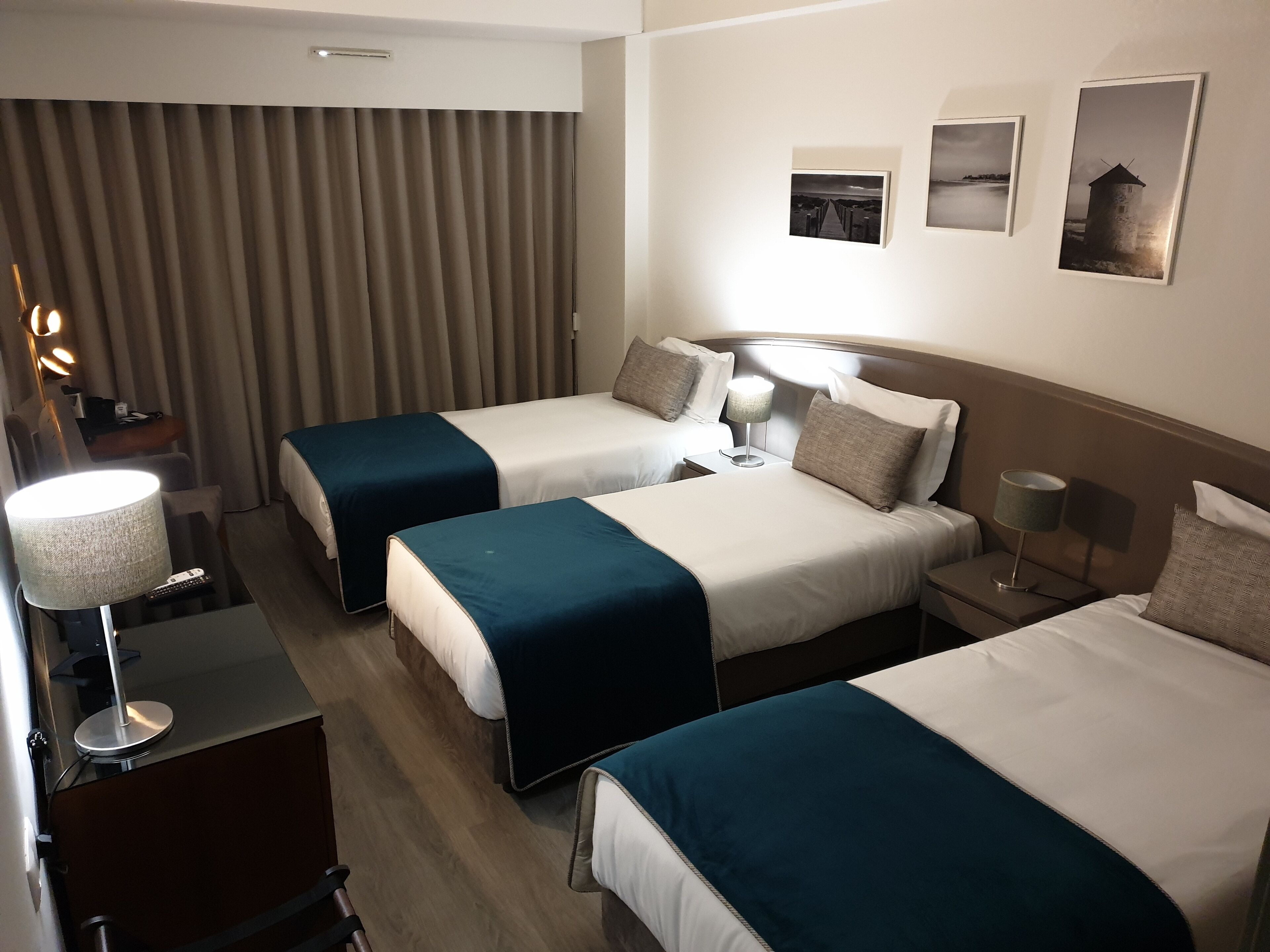 A hotel room with two beds, a desk with a lamp, a chair, and a curtain.