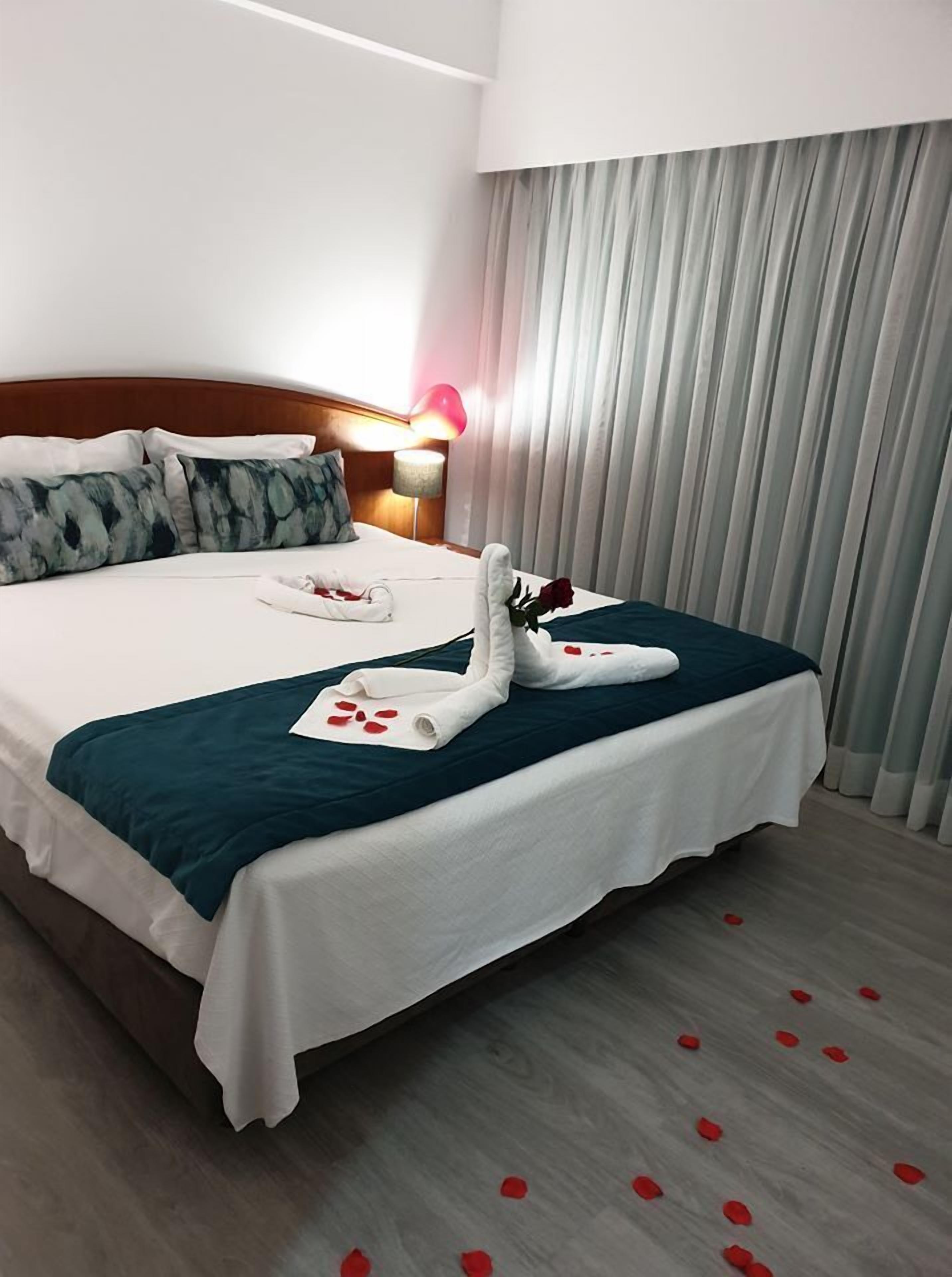 Una habitación de hotel con una cama bien hecha, una lámpara de noche y un ventanal con cortinas.