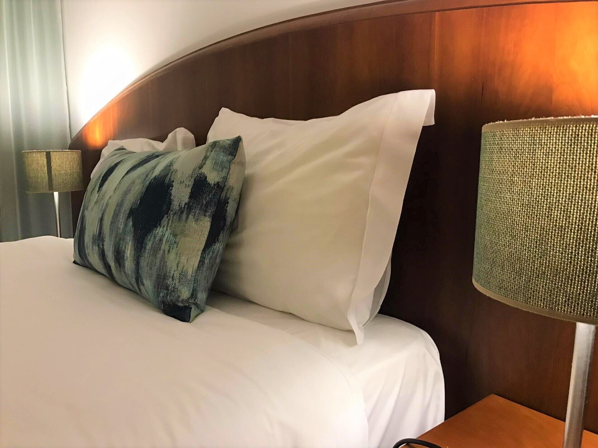 Une chambre d’hôtel avec un lit, des oreillers, une lampe et une tête de lit en bois.