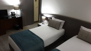 A hotel room with a bed, bedside table, lamp, and a desk with a coffee maker.