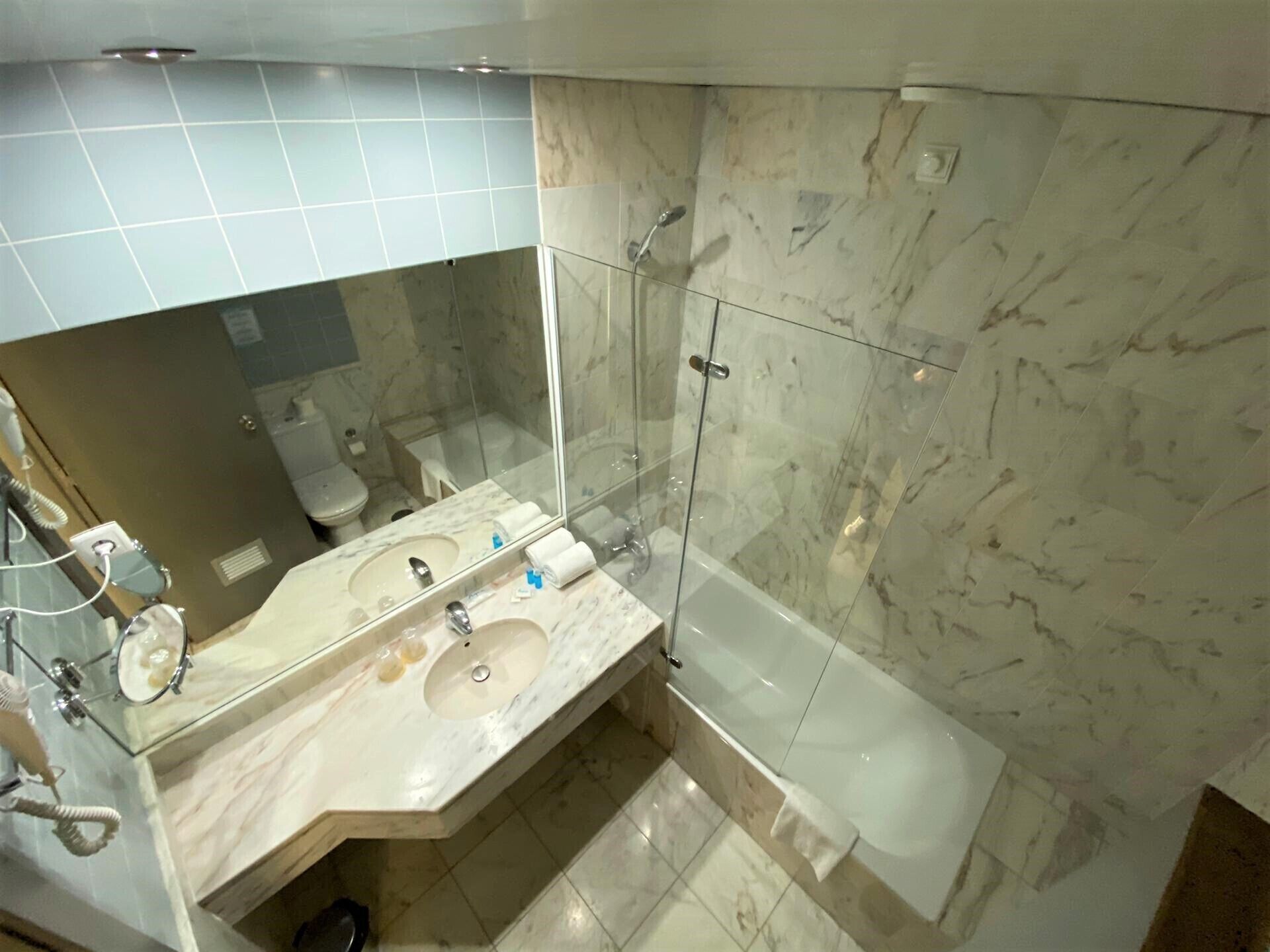 Un baño con lavamanos de mármol, ducha con cerramiento de vidrio y bañera.