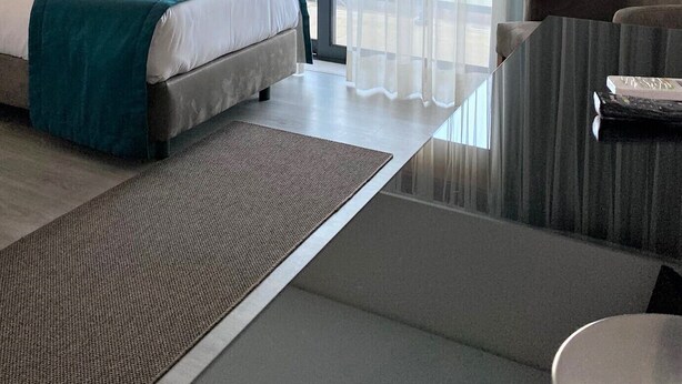 Une chambre d’hôtel moderne, dotée d’un grand lit, d’un canapé et offrant une vue sur le paysage urbain à travers de fines rideaux.