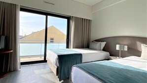Une chambre d’hôtel avec deux lits, un balcon et une vue sur un immeuble.