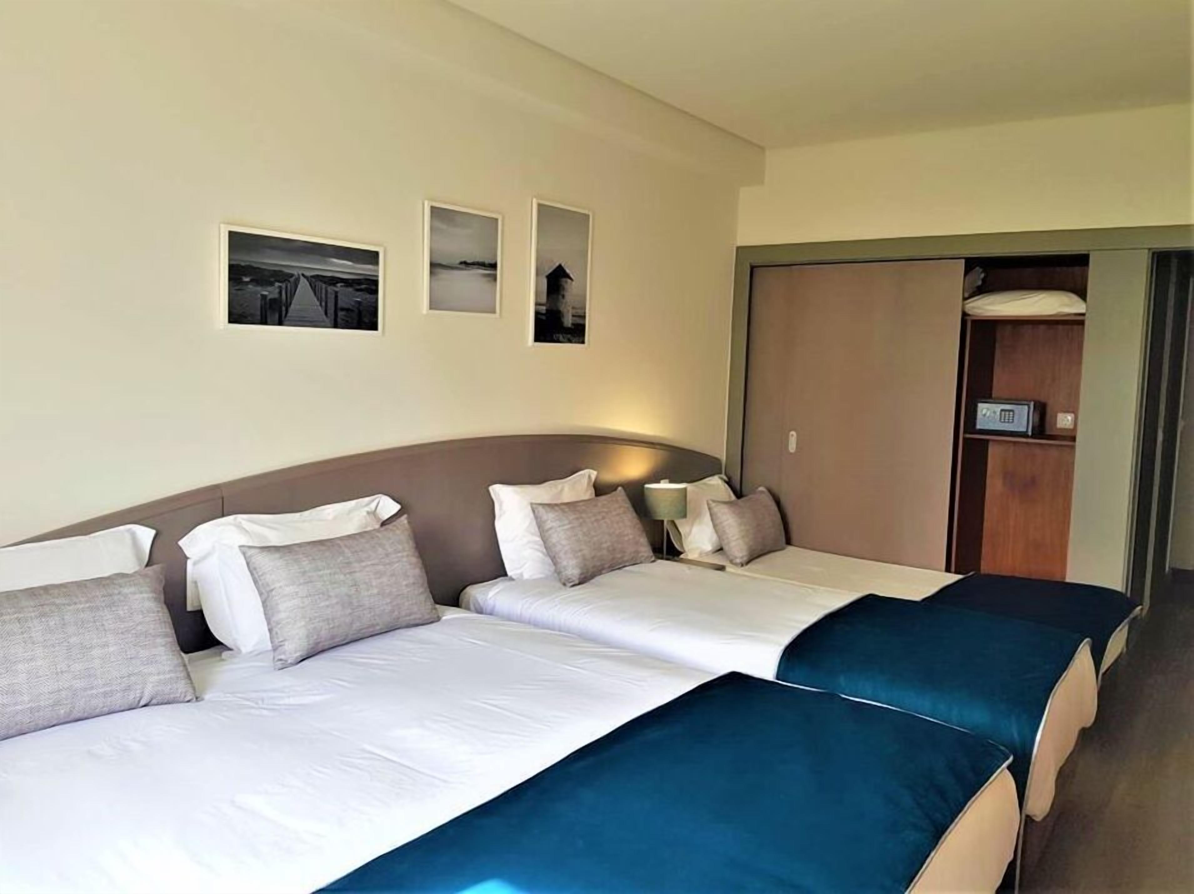 A hotel room with a large bed, a wardrobe, and three framed pictures on the wall.