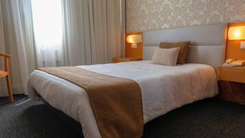 Ein Hotelzimmer mit einem großen Bett, einem Nachttisch aus Holz mit Telefon und einer Wandlampe.