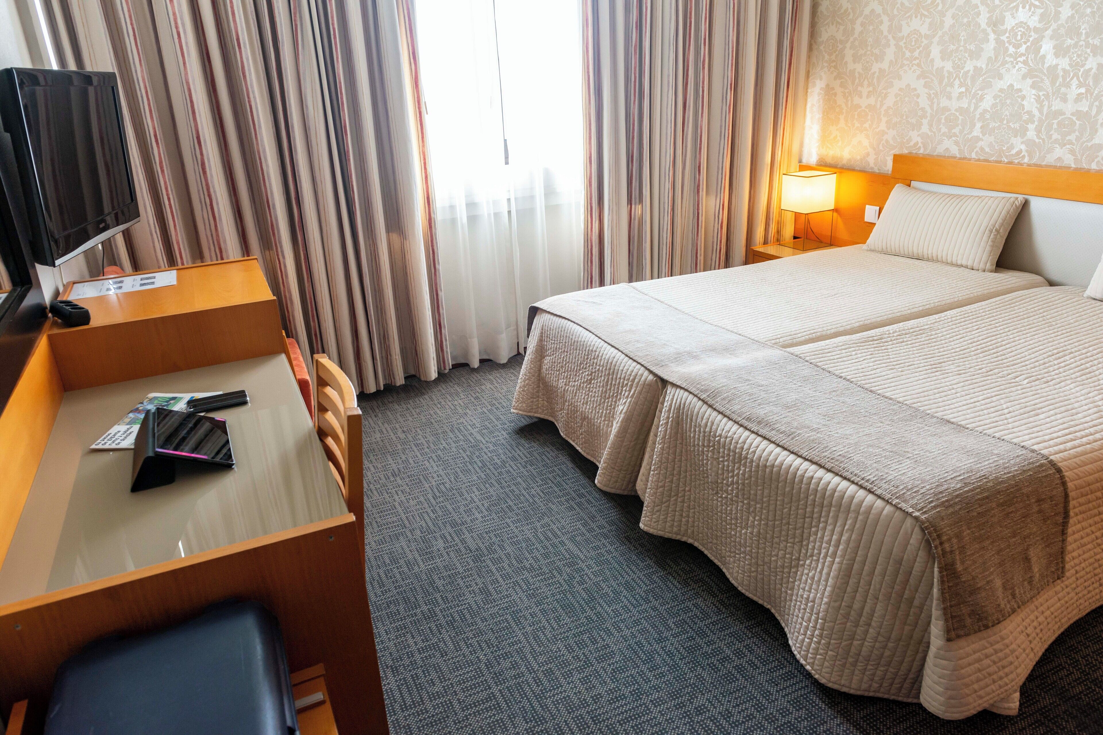 A hotel room with a bed, a desk with a chair, a TV, and a lamp.