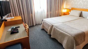 A hotel room with a bed, a desk with a chair, a TV, and a lamp.