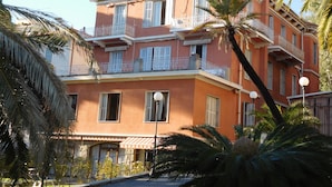 A multi-story building with balconies, a red facade, and palm trees. - Hotel Villa Maria (Sanremo)