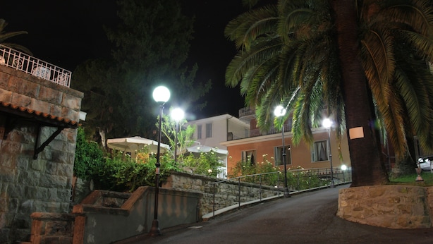 A nighttime street scene with stone walls, a metal railing, and a street lamp. - Hotel Villa Maria (Sanremo)