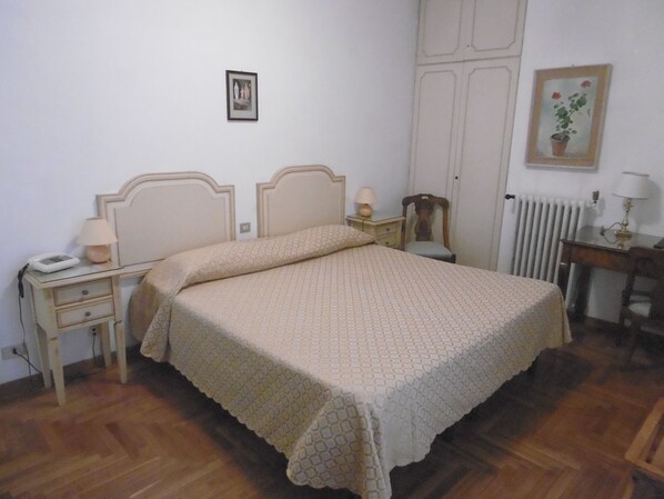A bedroom with a bed, bedside tables, a nightstand, a chair, a radiator, and a picture on the wall. - Hotel Villa Maria (Sanremo)