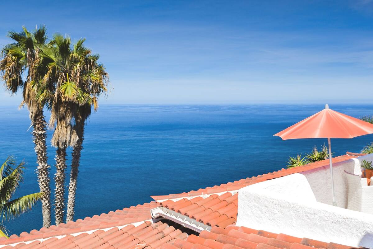 Una terraza con una sombrilla roja, paredes blancas y vista al mar.