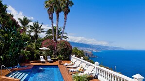 A pool area with lounge chairs and a view of the ocean.
