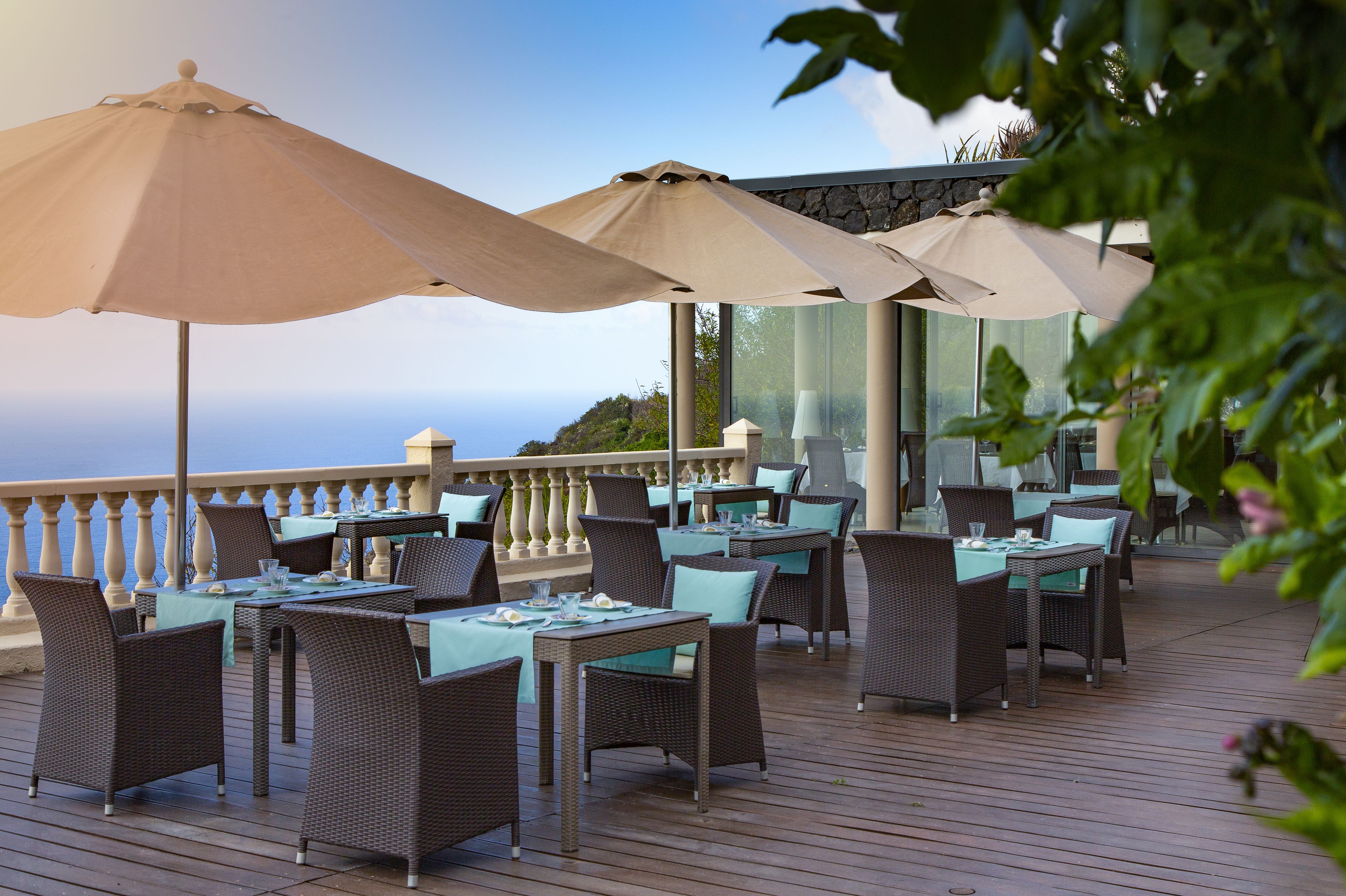 Een terras met tafels en stoelen, parasols en uitzicht op de oceaan.
