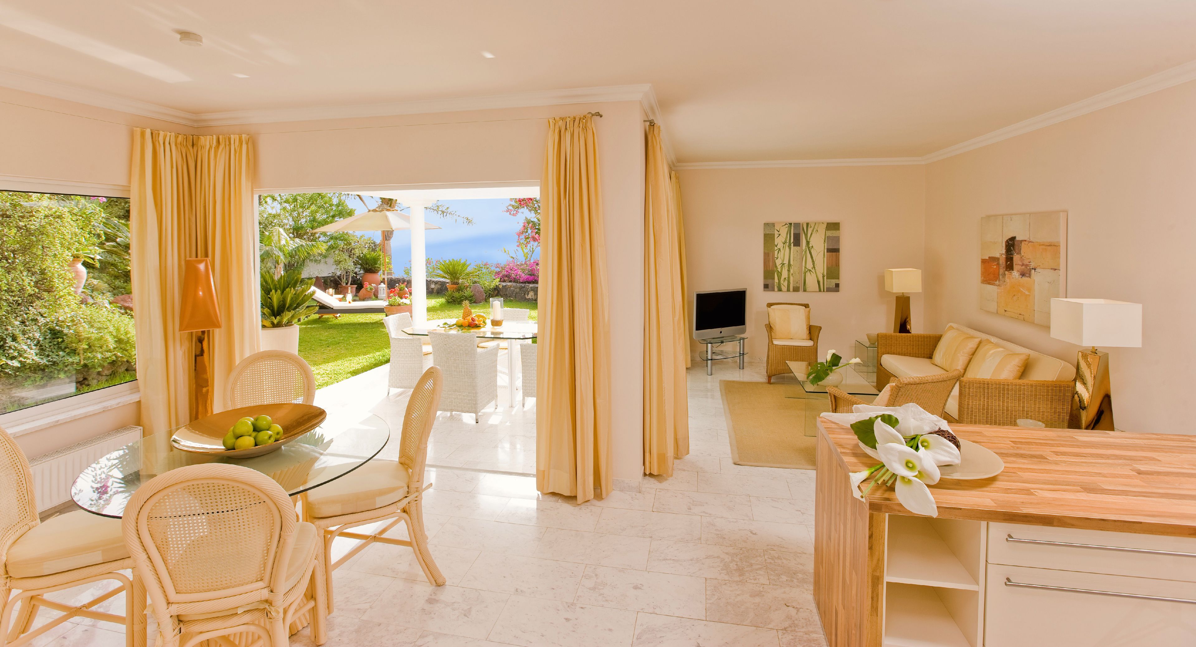 Ein geräumiger Wohnbereich mit Glastisch, Korbstühlen, einer Couch und Blick auf Garten und Meer.