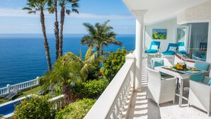 A balcony with white wicker furniture, a pool, and a view of the ocean.