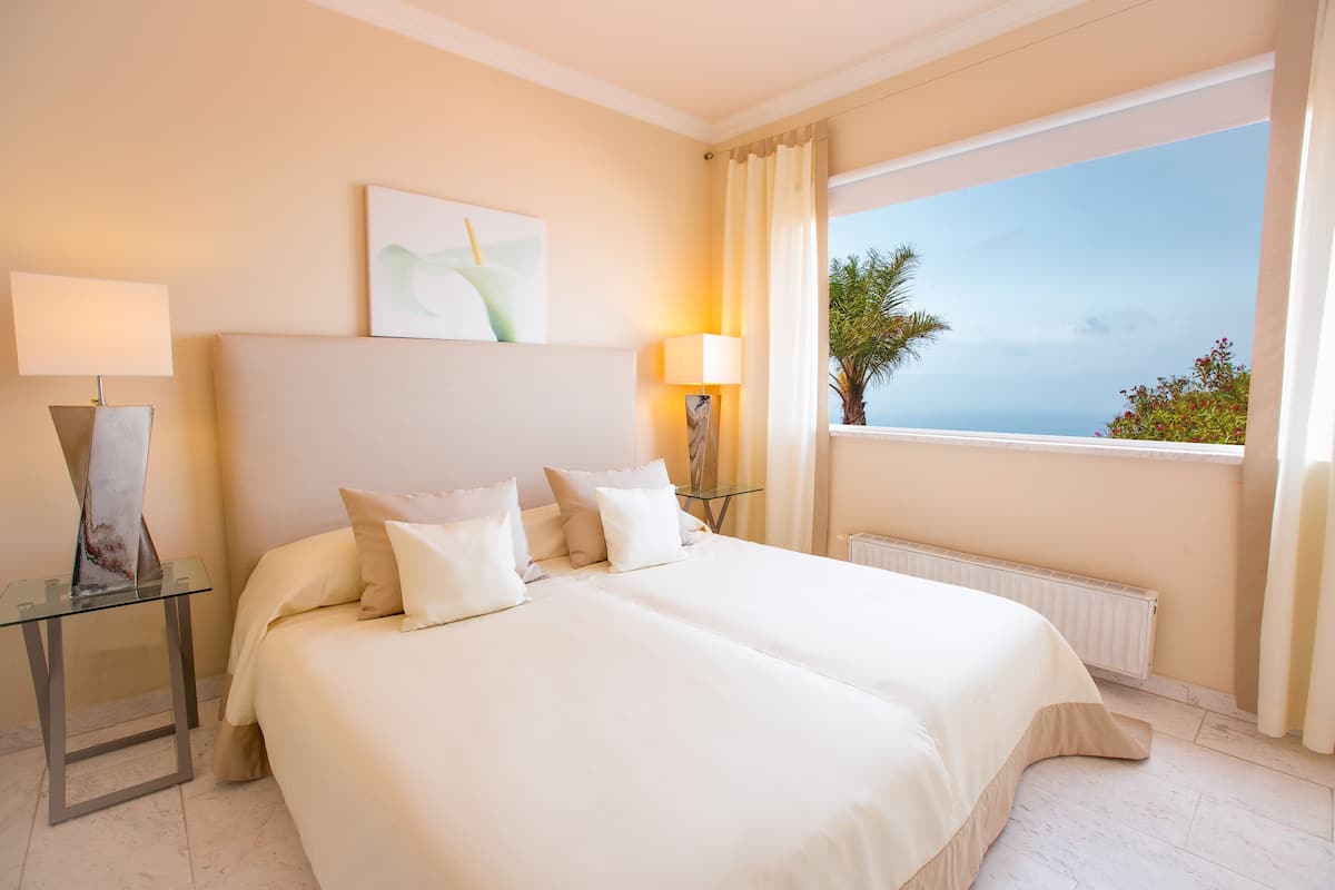 Habitación de hotel con una cama grande, dos lámparas de noche, una mesita de cristal y vistas al mar.