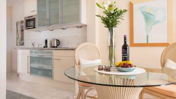 A modern kitchen with a glass dining table, wicker chairs, and a vase with flowers.