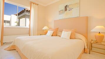A large bed with a headboard, two bedside tables with lamps, a window with curtains, and a painting on the wall.