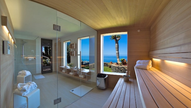 A modern spa room with a glass wall, a wooden bench, and a view of the ocean.