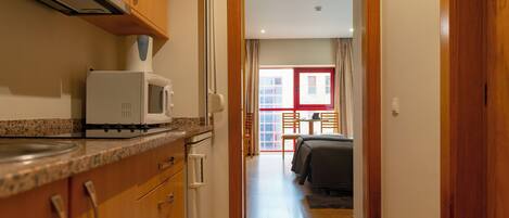 Un pasillo estrecho que conduce a un dormitorio con cama, una zona de comedor con mesa y sillas, y una cocina con microondas y armarios.