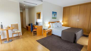 A hotel room with a bed, a desk with a chair, a nightstand with a lamp, and a wardrobe.