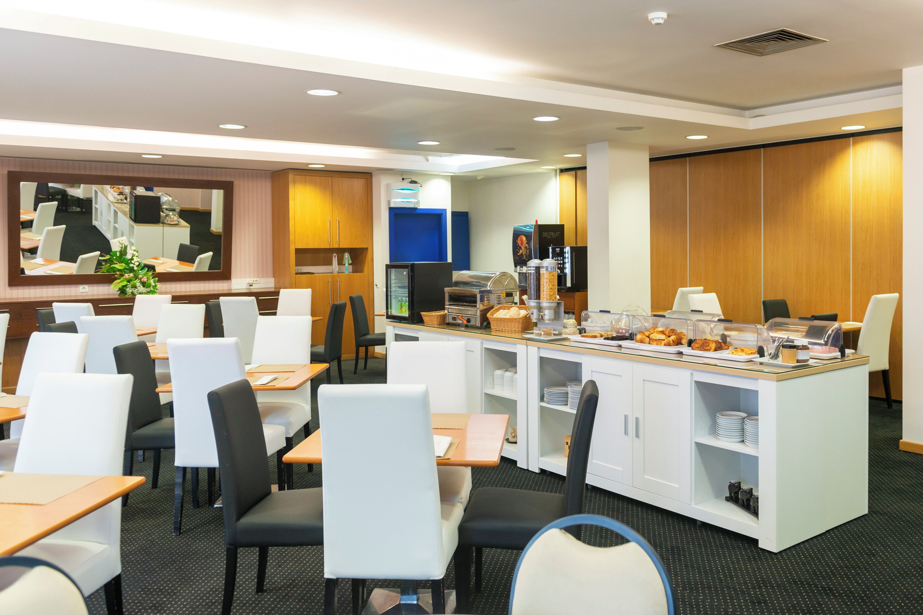 Uma área de refeições de hotel com mesas, cadeiras, um buffet e um espelho grande.