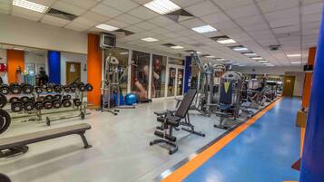 Un gimnasio con diverso equipo de ejercicio, una banca y suelo azul anaranjado.