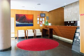 A reception area with a wooden reception desk, a red carpet, white chairs, and a large painting on the wall.