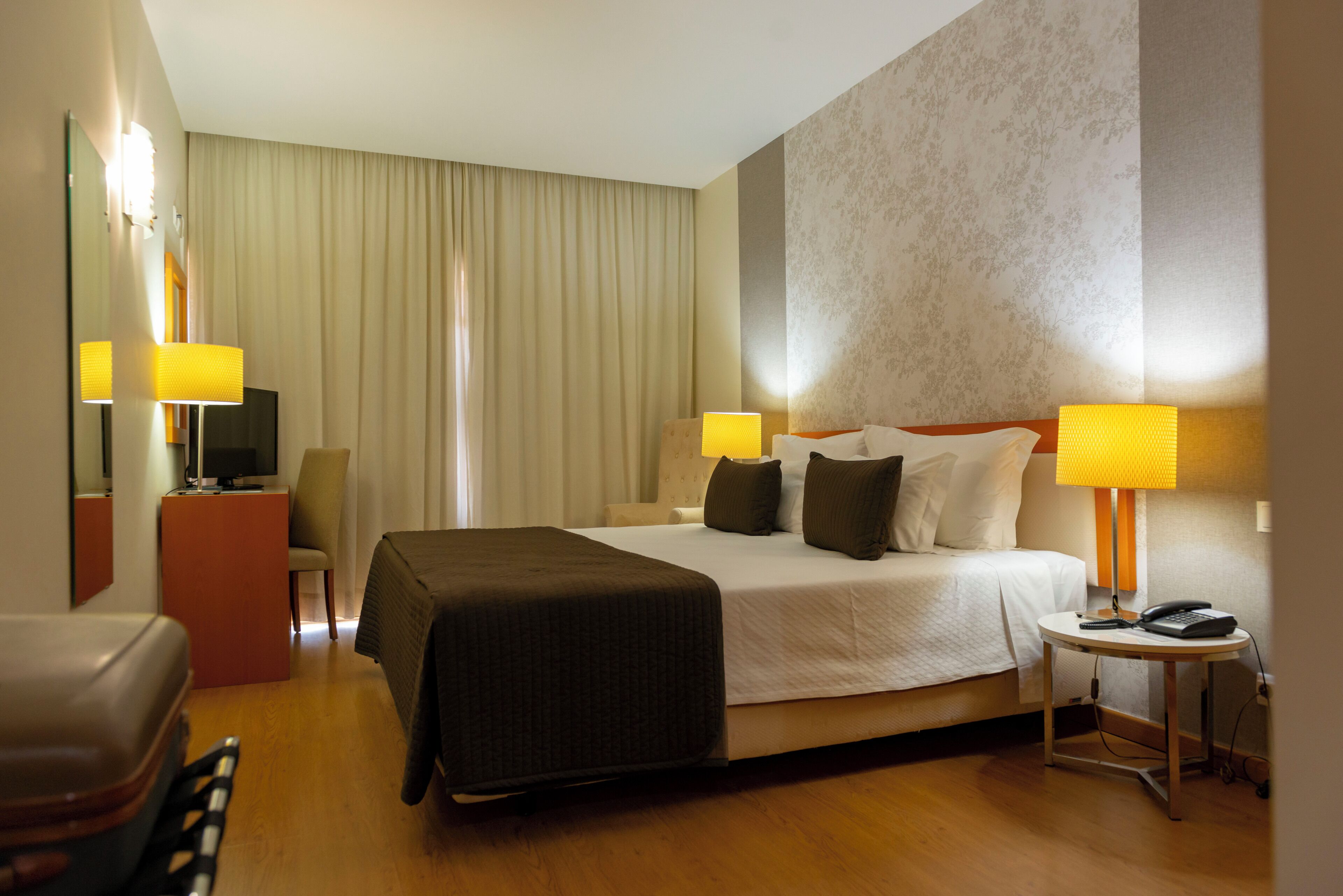A hotel room with a bed, bedside lamps, a desk, a chair, and a telephone.
