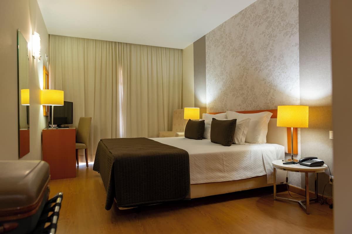A hotel room with a bed, bedside lamps, a desk, a chair, and a telephone.