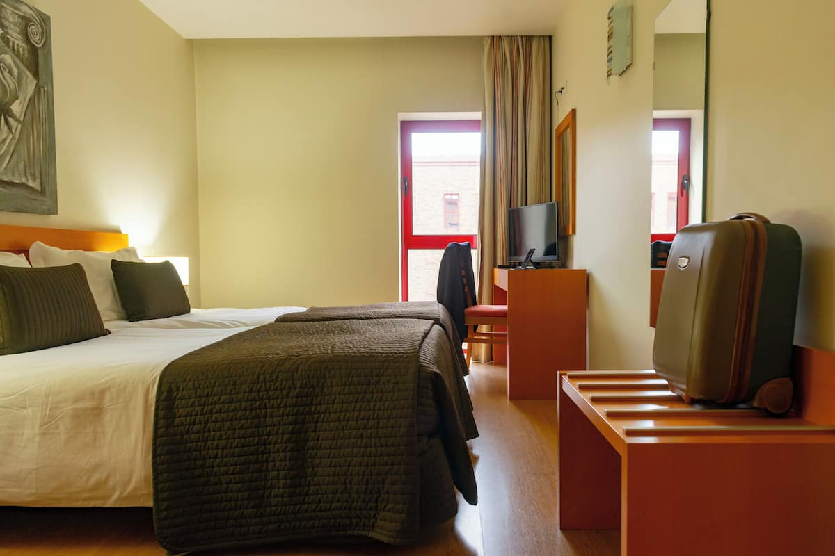 Una habitación de hotel con una cama, un escritorio con televisor y una maleta sobre un atril.