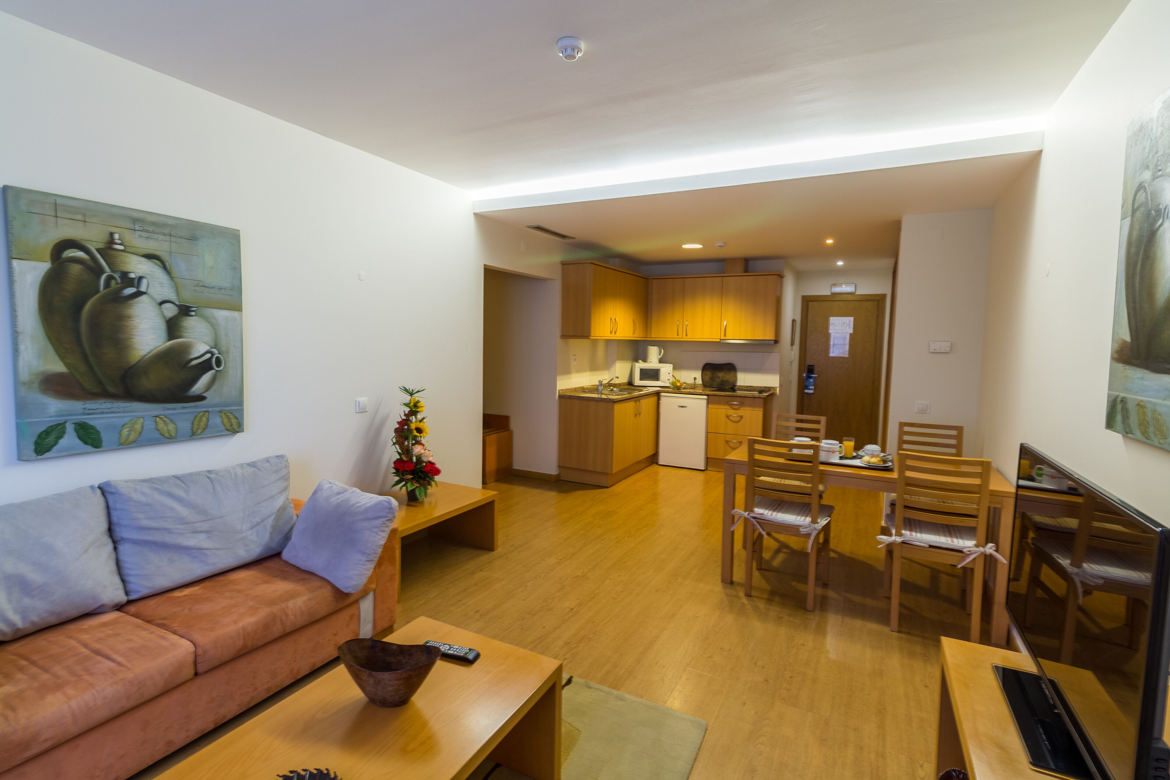 Un espacio habitable compacto con sofá, mesa de comedor, sillas, zona de cocina y obras de arte en las paredes.