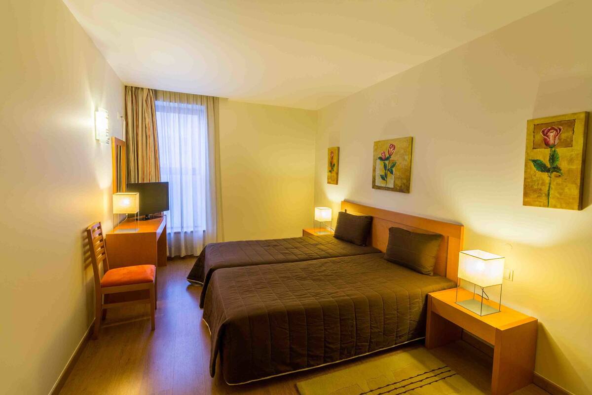 Habitación de hotel con dos camas, un escritorio con silla, un televisor y obras de arte en las paredes.