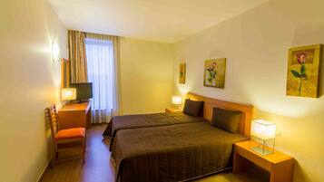 A hotel room with two beds, a desk with a chair, a TV, and artwork on the walls.
