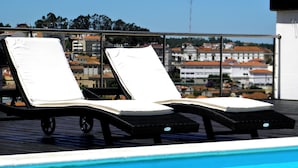 Zona junto a la piscina con dos sillas reclinables y vista despejada a edificios al fondo.
