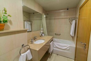 A modern bathroom with a beige sink, a mirror, a shower with a glass door, and a wooden door.