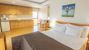 Habitación de hotel con cama, escritorio, silla, kitchenette pequeño y un cuadro en la pared.